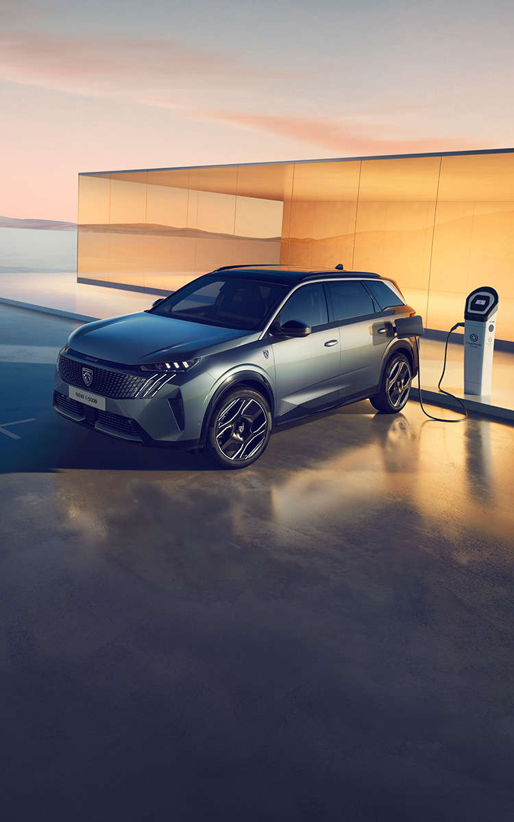 Peugeot e-5008 синього кольору заряджається від електромережі, вигляд спереду з лівого боку